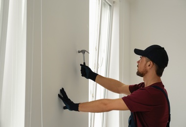 Photo of Handyman in uniform working with hammer indoors. Professional construction tools