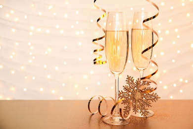 Photo of Glasses of champagne and decorative snowflake on table against blurred Christmas lights