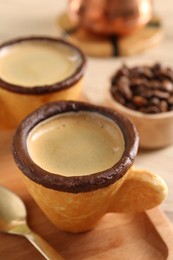 Photo of Delicious edible biscuit cups with espresso, spoon and board on table, closeup
