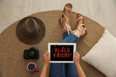 Photo of Woman using tablet with Black Friday announcement while sitting on floor at home, above view