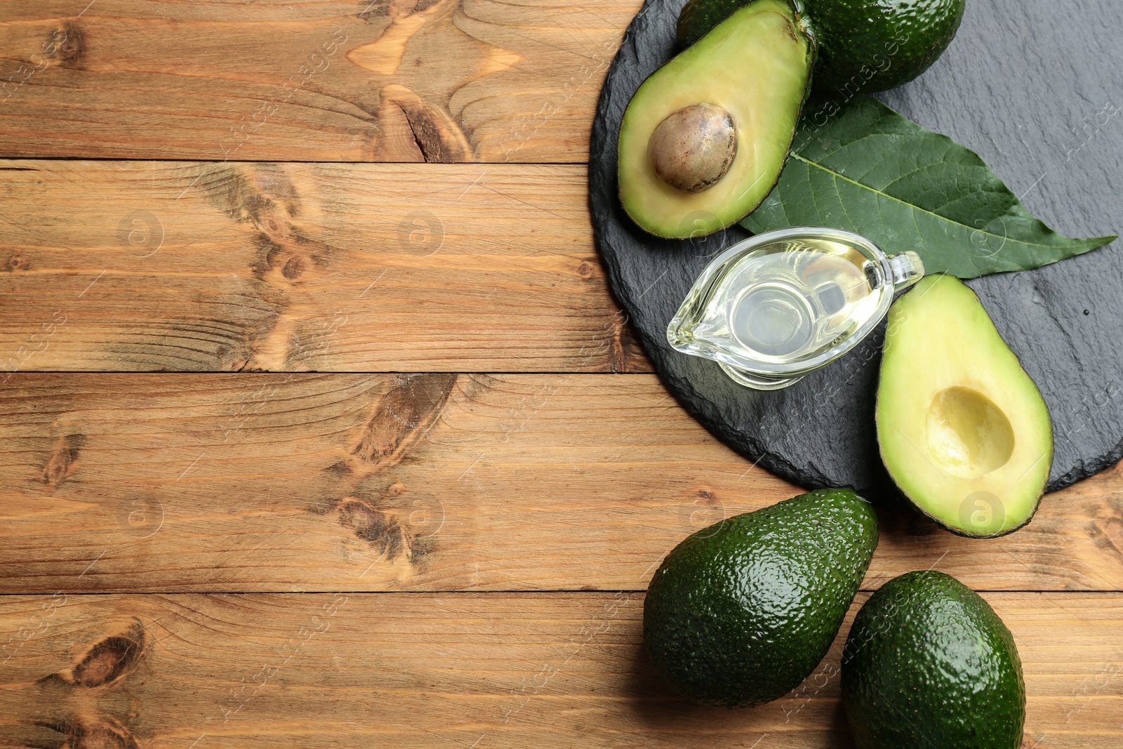 Photo of Composition with natural oil and avocados on wooden background, flat lay. Space for text