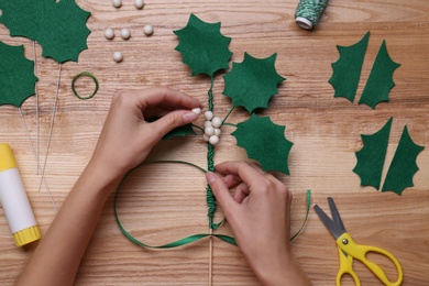 Photo of Woman making mistletoe branch at wooden table, top view