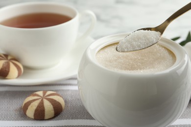 Photo of Spoon with granulated sugar over bowl on table