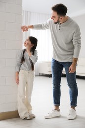 Photo of Father measuring daughter's height near white brick pillar at home