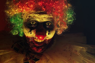 Photo of Terrifying clown in darkness, closeup. Halloween party costume