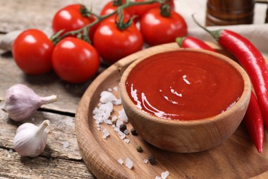 Photo of Delicious ketchup in bowl, chili pepper and spices on wooden table, closeup. Tomato sauce