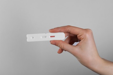 Photo of Woman holding disposable Covid-19 express test on light grey background, closeup