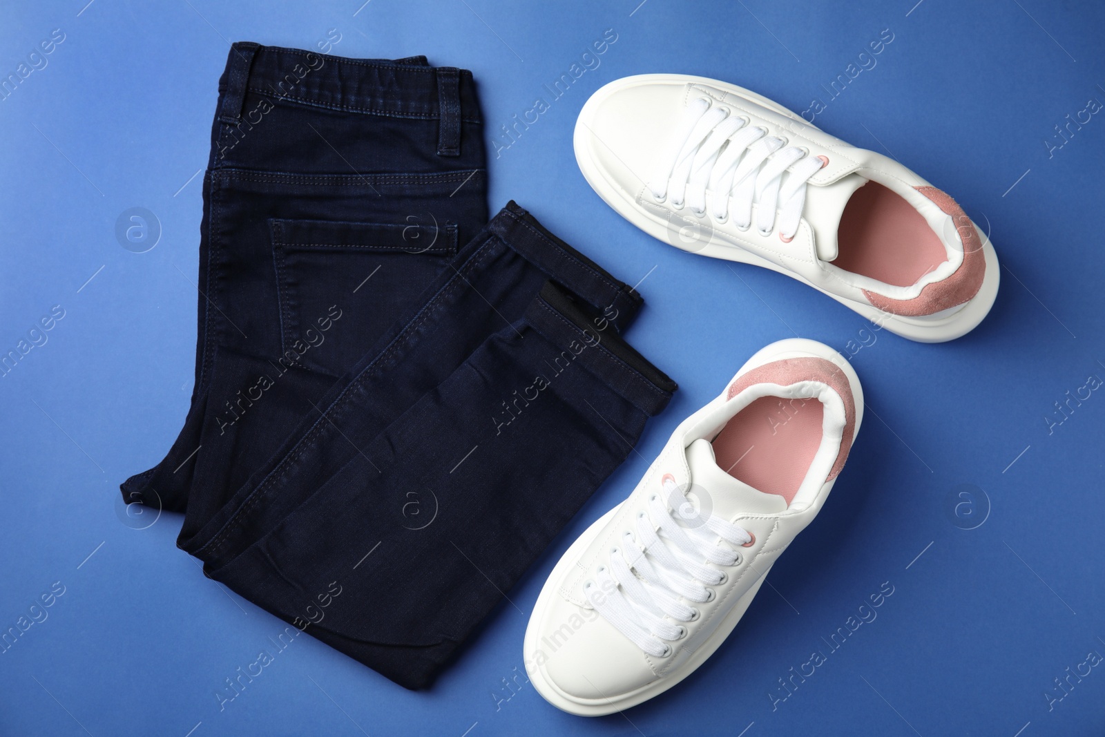 Photo of Stylish white sneakers and jeans on blue background, flat lay