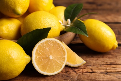 Photo of Many fresh ripe lemons with green leaves on wooden table, closeup