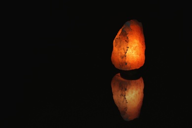 Photo of Himalayan salt lamp on black background. Space for text