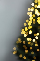 Photo of Blurred view of beautiful fir tree with Christmas lights on grey background, space for text