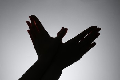 Photo of Shadow puppet. Woman making hand gesture like bird on grey background, closeup