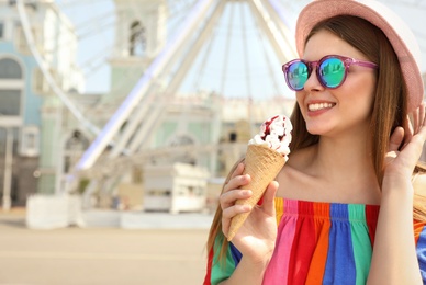 Photo of Young happy woman with ice cream cone in amusement park. Space for text