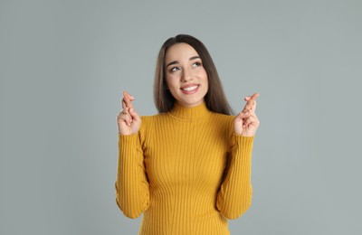 Photo of Excited young woman holding fingers crossed on grey background. Superstition for good luck