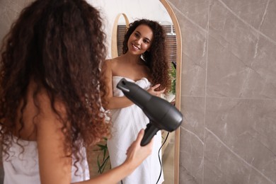 Photo of Beautiful African American woman using hair dryer near mirror in bathroom, space for text