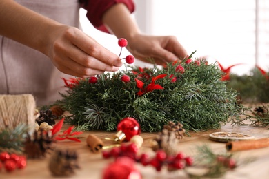 Photo of Florist making beautiful Christmas wreath with berries at wooden table indoors, closeup