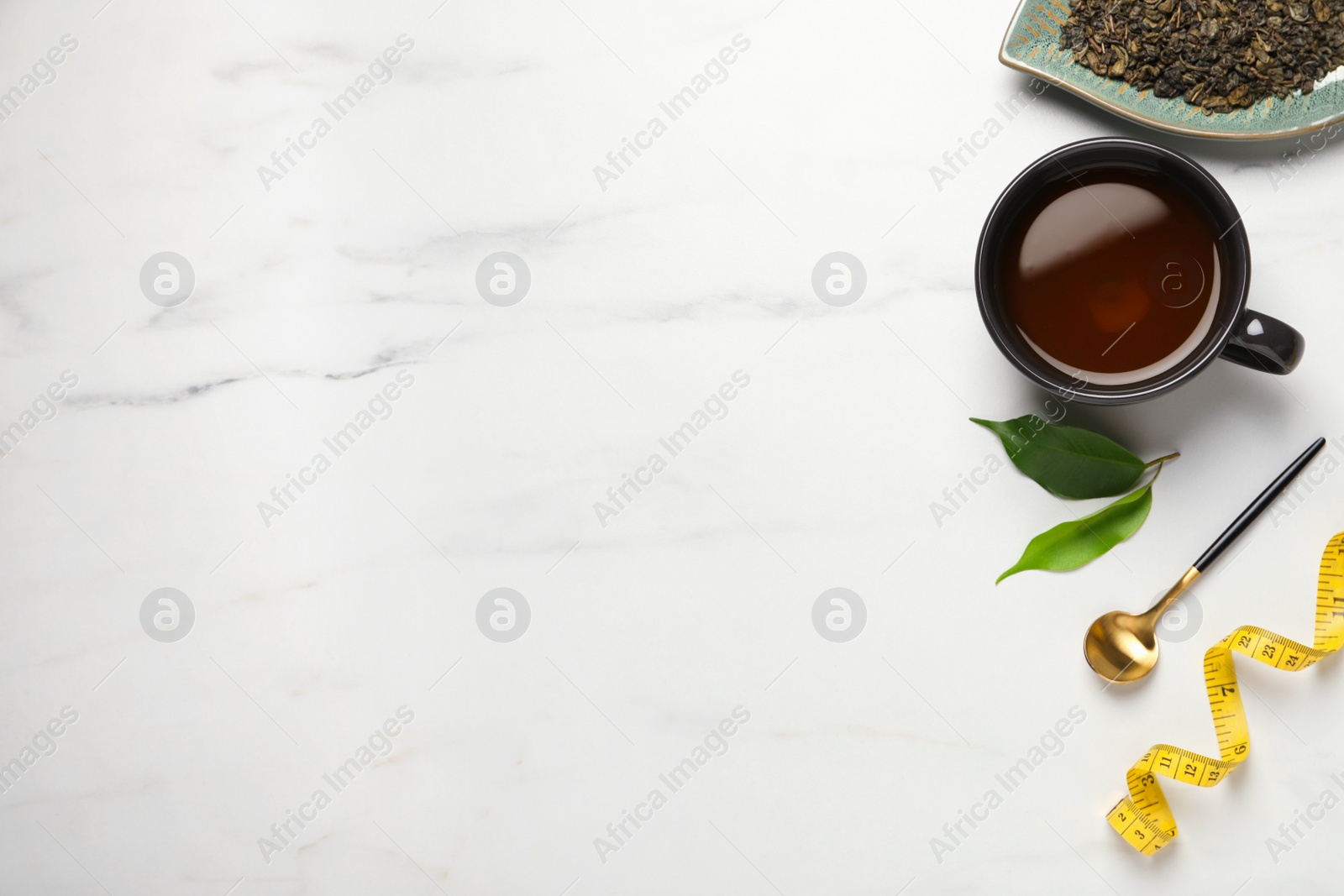 Photo of Flat lay composition with herbal diet tea, spoon and measuring tape on white marble table, space for text. Weight loss concept