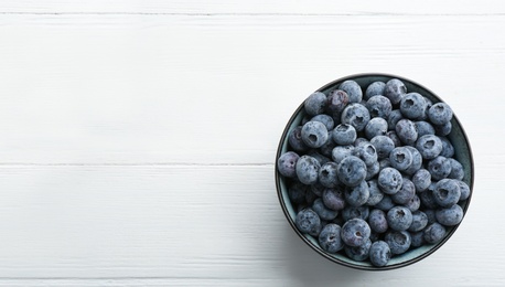 Photo of Tasty frozen blueberries in bowl on white wooden table, top view. Space for text