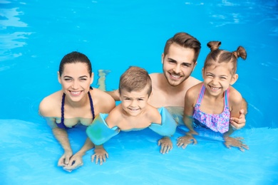 Photo of Young family with little children in swimming pool on sunny day