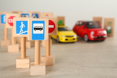 Photo of Many different miniature road signs and cars on wooden table, space for text. Driving school