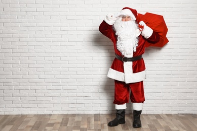 Photo of Authentic Santa Claus with bag full of gifts against white brick wall. Space for text