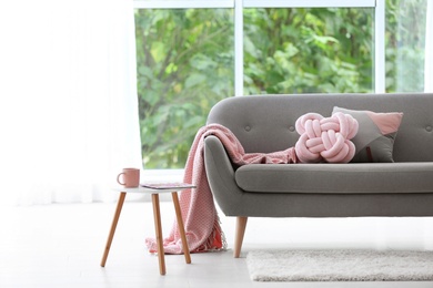 Photo of Pillows and plaid on sofa in living room interior. Unusual cushion design