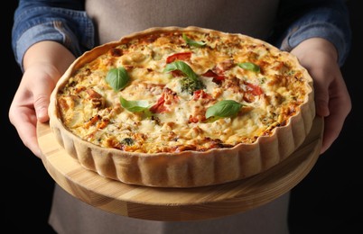 Photo of Woman holding board with tasty quiche on black background, closeup