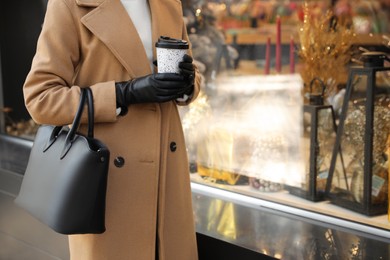 Photo of Woman with stylish leather gloves and cup of coffee outdoors, closeup