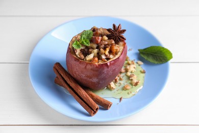 Photo of Tasty baked apple with nuts, honey, spices and mint on white wooden table