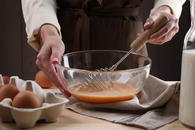 Photo of Woman whisking eggs in bowl at table, closeup