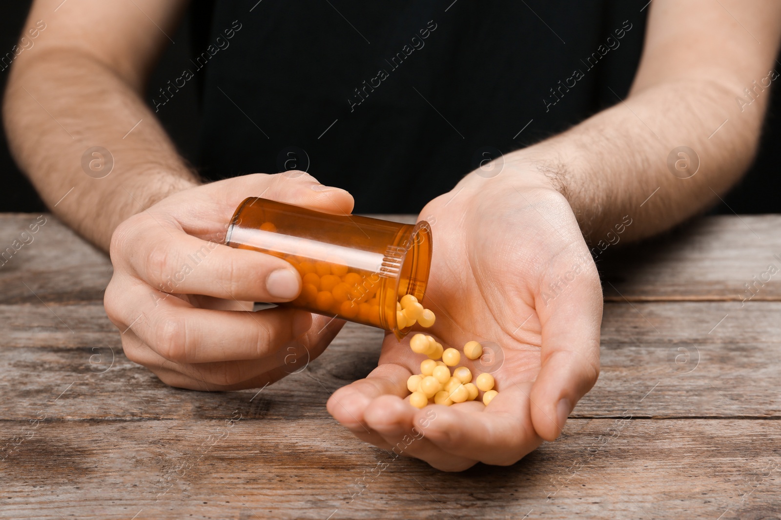 Photo of Man pouring pills out of bottle into hand at table, closeup