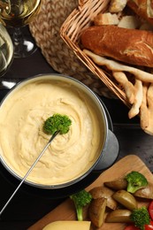 Photo of Dipping piece of broccoli into fondue pot with melted cheese at table with snacks, flat lay