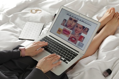 Photo of Woman holding laptop with open beauty blogger site on bed, closeup