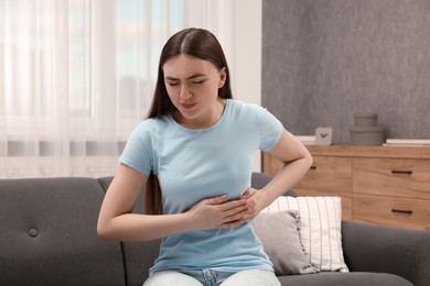 Photo of Woman suffering from stomach pain on sofa indoors