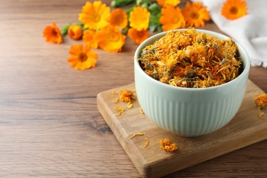 Photo of Bowl of dry calendula flowers on wooden table. Space for text