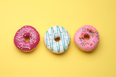 Photo of Tasty glazed donuts on yellow background, flat lay