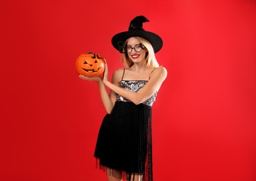 Photo of Beautiful woman in witch costume with jack o'lantern on red background. Halloween party