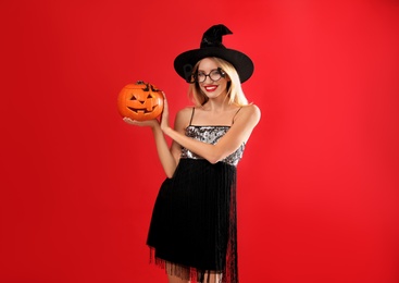 Beautiful woman in witch costume with jack o'lantern on red background. Halloween party