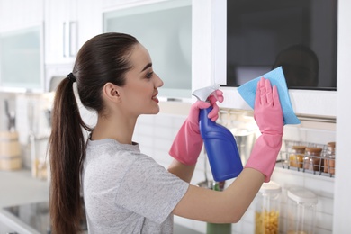 Photo of Young woman cleaning microwave oven with rag at home