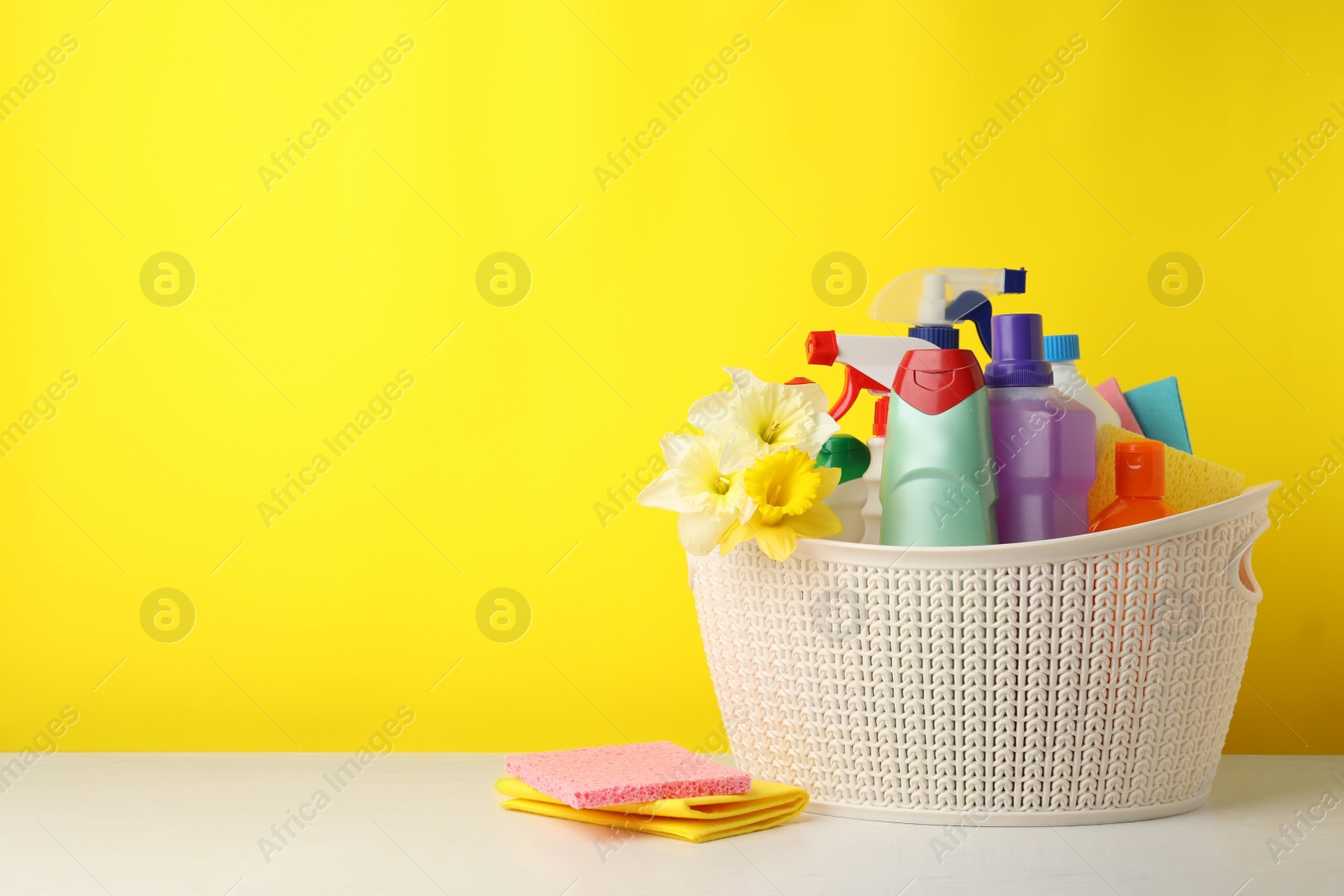 Photo of Plastic basket with spring flowers and cleaning supplies on wooden table. Space for text