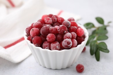 Photo of Frozen red cranberries in bowl and green leaves on light table, closeup