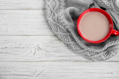 Photo of Cup of hot cocoa and knitted sweater on white wooden table, top view with space for text. Winter drink