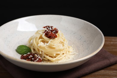 Tasty spaghetti with sun-dried tomatoes and parmesan cheese on wooden table, closeup. Exquisite presentation of pasta dish
