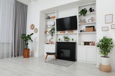 Photo of Stylish room interior with beautiful fireplace, TV set and shelves with decor and houseplants