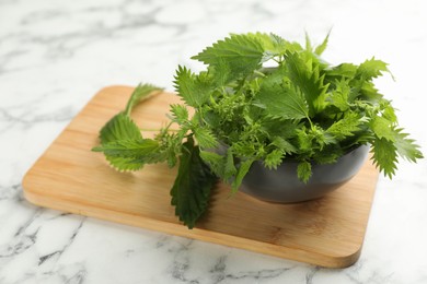 Photo of Fresh stinging nettle leaves on white marble table, closeup