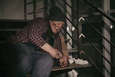 Photo of Poor senior man counting coins on stairs indoors