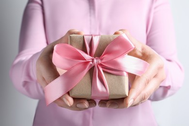 Photo of Woman holding gift box with pink bow on light grey background, closeup