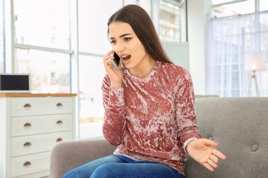 Photo of Young woman talking on mobile phone at home