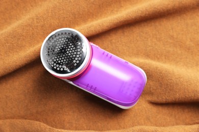 Photo of Modern fabric shaver on brown cloth, top view