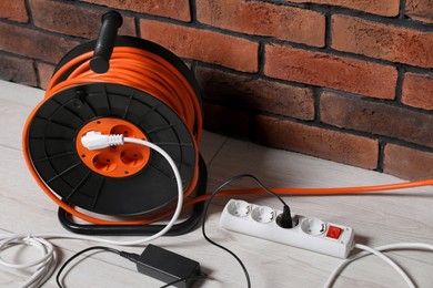Photo of Extension cord reel on white floor near brick wall. Electrician's equipment